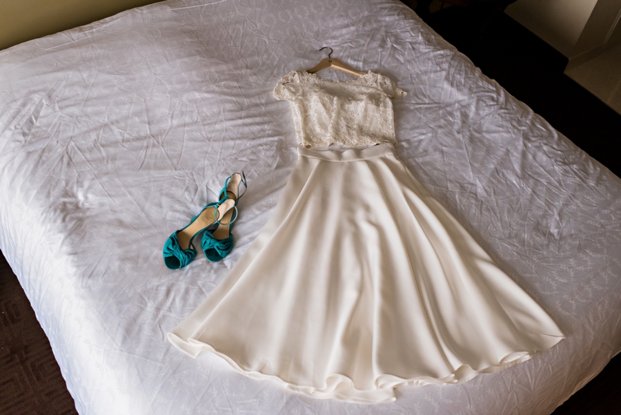 A two piece wedding dress and and blue shoes laying on a hotel bed in Philadelphia.